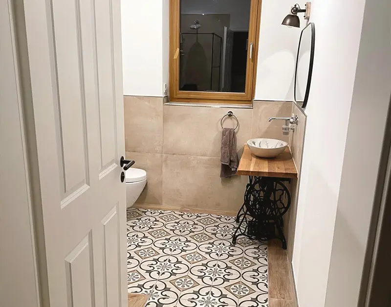 einfamilienhaus-neubau-badezimmer-kirk-bau-01 Modernes Badezimmer mit gemusterten Bodenfliesen, Holzwaschtisch und wandhängendem WC.