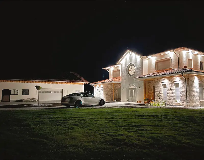 einfamilienhaus-neubau-nachtansicht-kirk-bau-01 Beleuchtetes Einfamilienhaus mit Garage und Klinkerfassade bei Nacht.