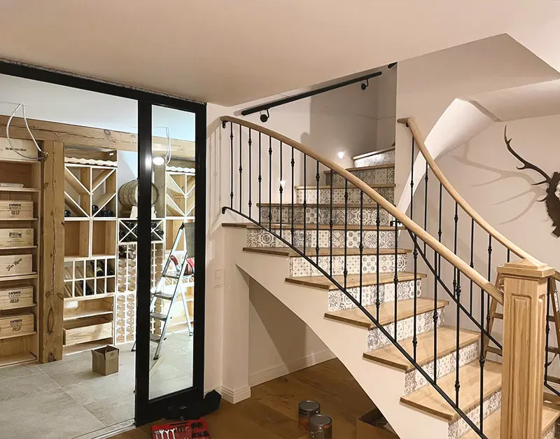 einfamilienhaus-neubau-treppenanlage-kirk-bau-01 Individuelle Innentreppe mit Holzstufen, gemusterten Fliesen und schwarzem Metallgeländer.