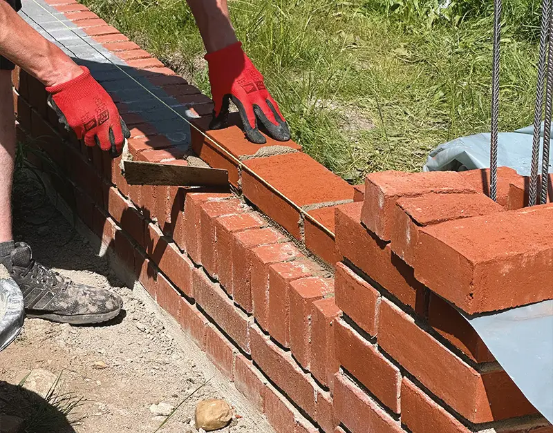 mauerwerksarbeiten-klinker-kirk-bau-02 Maurer setzt rote Klinkersteine auf eine frisch gemauerte Außenwand.