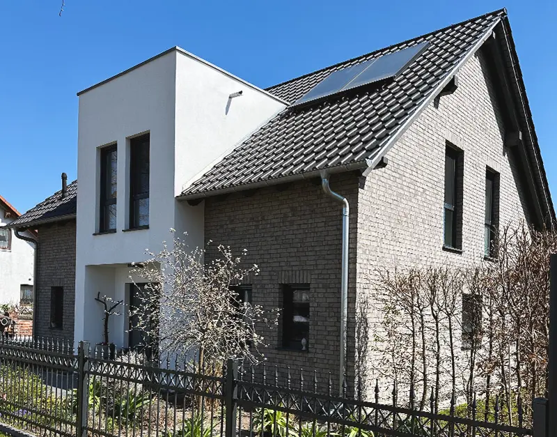 modernes-einfamilienhaus-klinkerfassade-seitenansicht-kirk-bau-01 Seitenansicht eines modernen Wohnhauses mit grauer Klinkerfassade und schwarzem Satteldach.