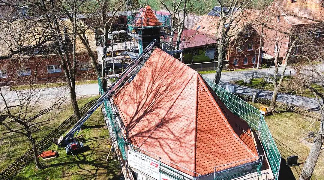 sanierung-historischer-gebaeudeturm-kirk-bau-01 Drohnenaufnahme eines historischen Gebäudes mit eingerüstetem Turm während der Dach- und Sanierungsarbeiten.